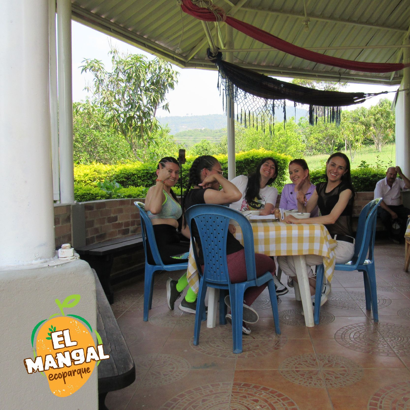 Grupo de personas sentadas en una mesa al aire libre, sonriendo, bajo un patio cubierto.