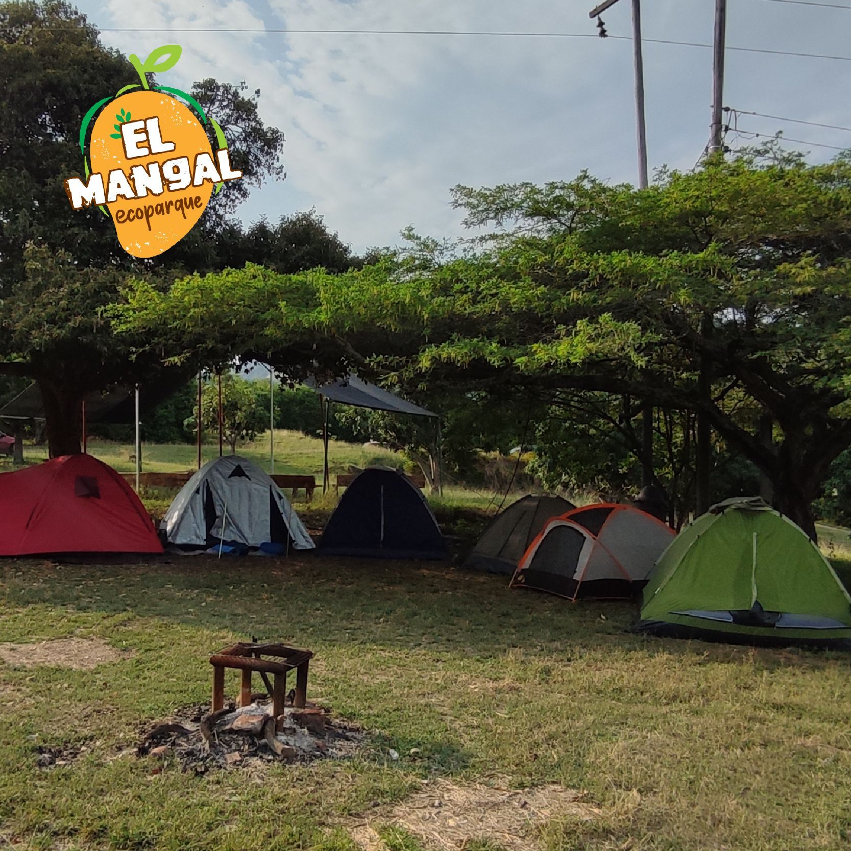 Tiendas de campaña instaladas en un campo de hierba en el Ecoparque El Mangal, bajo un cielo parcialmente nublado.