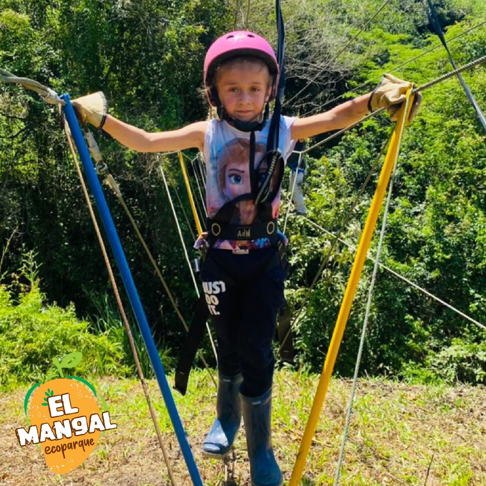 Joven con equipo de seguridad en una carrera de obstáculos, con los brazos extendidos sujetando postes. Casco rosa, al aire libre.