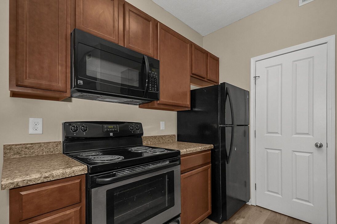 Small kitchen with black appliances, wood cabinets, granite counters, and a white pantry door.