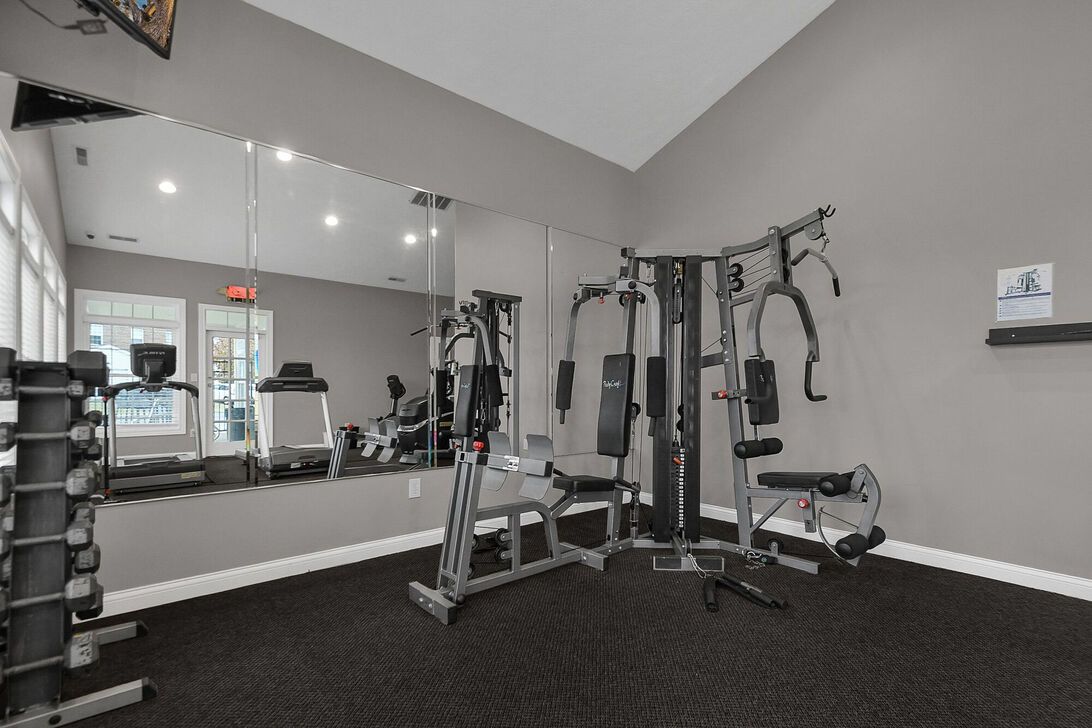 Small gym room with cable machine, dumbbells, mirror wall, and black carpet flooring.