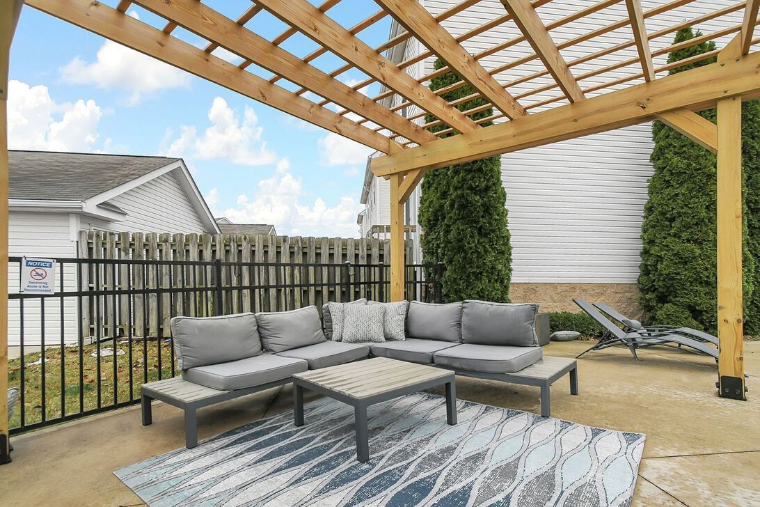 Patio seating area with gray sectional under a wooden pergola and patterned outdoor rug