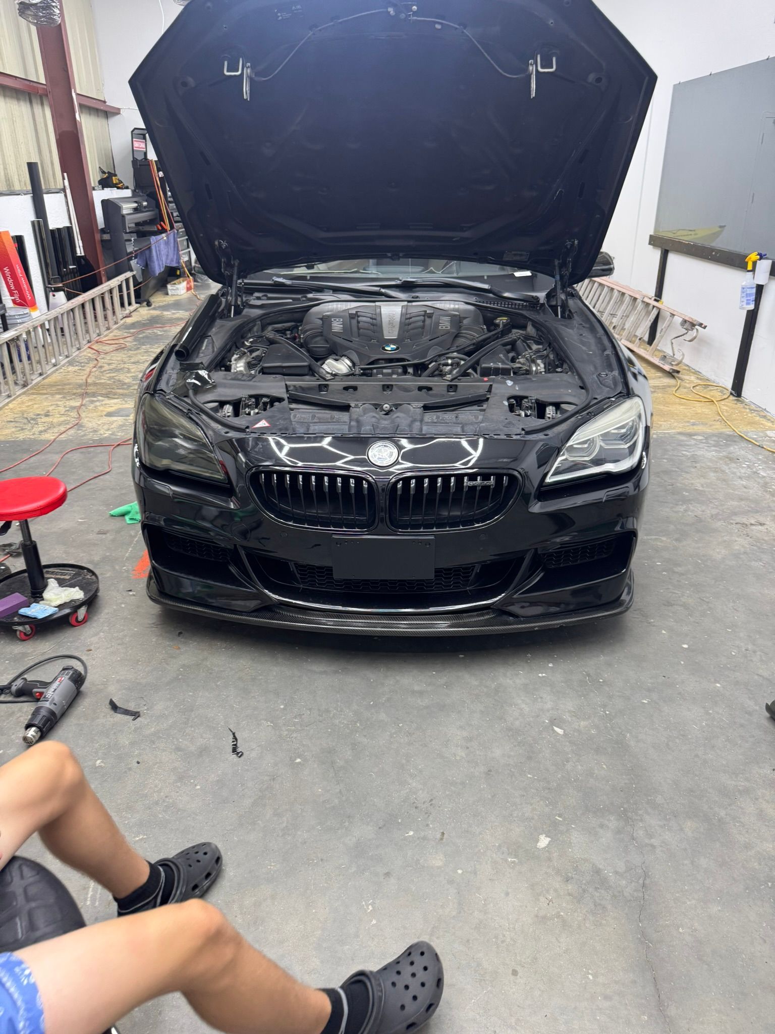 Black sports car with hood open in a garage, exposing the engine.