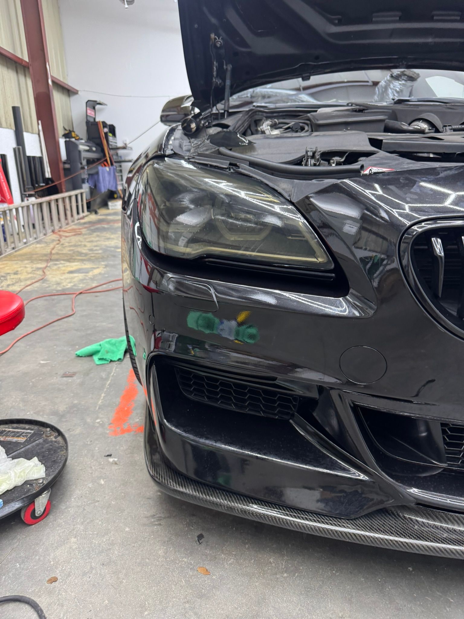 Black sports car front end in a garage, with hood open and workshop tools nearby