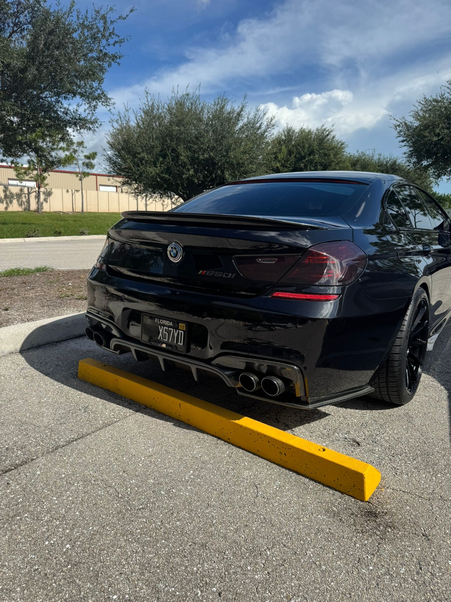 Black sedan backed into a yellow parking curb in a sunny outdoor lot.