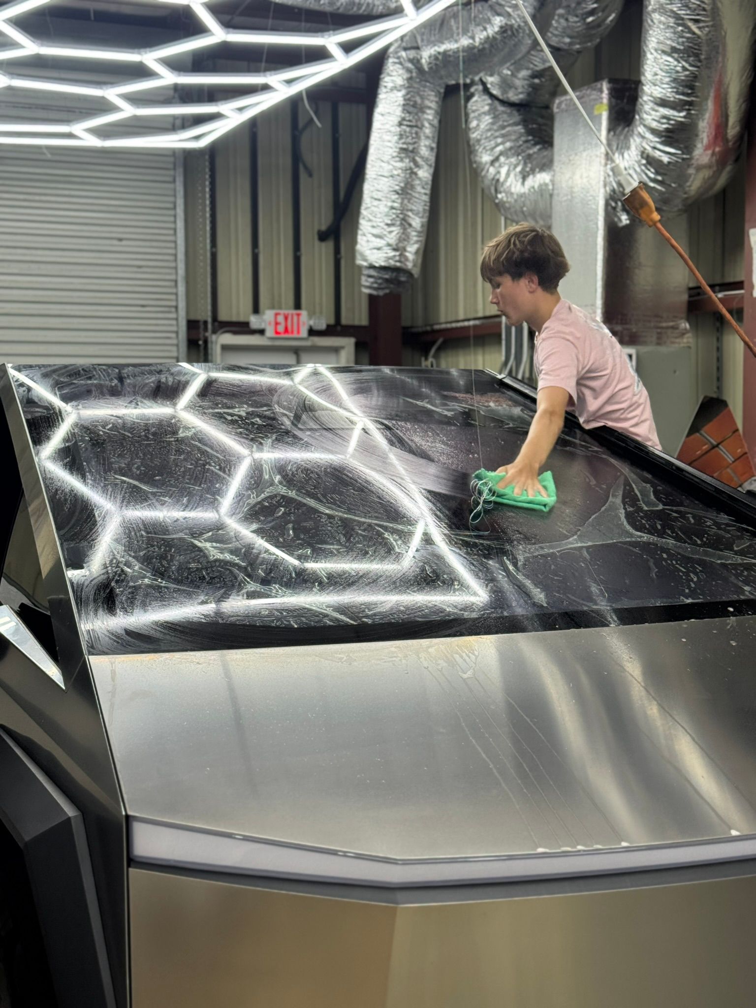 Person cleaning a large metallic machine surface in an industrial workshop under bright overhead lights