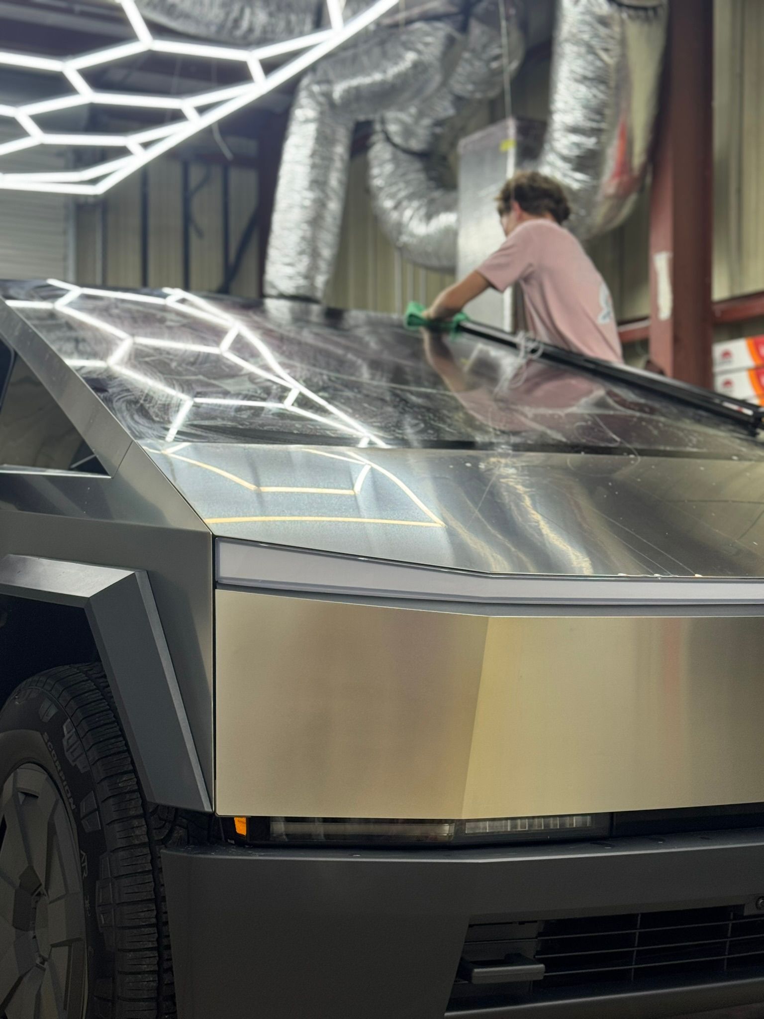 Person cleaning a silver Cybertruck under bright showroom lights