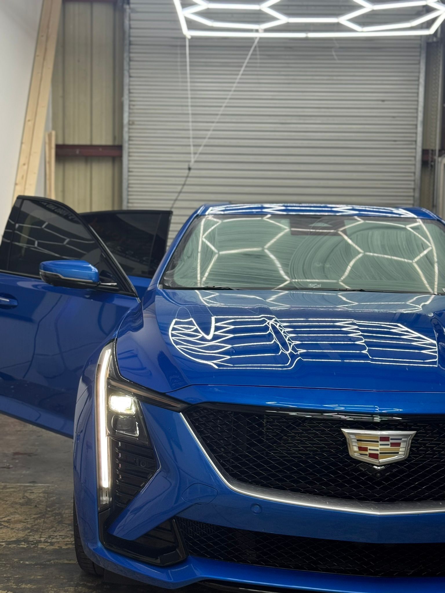 Blue Cadillac with driver's door open in a garage under bright overhead lights