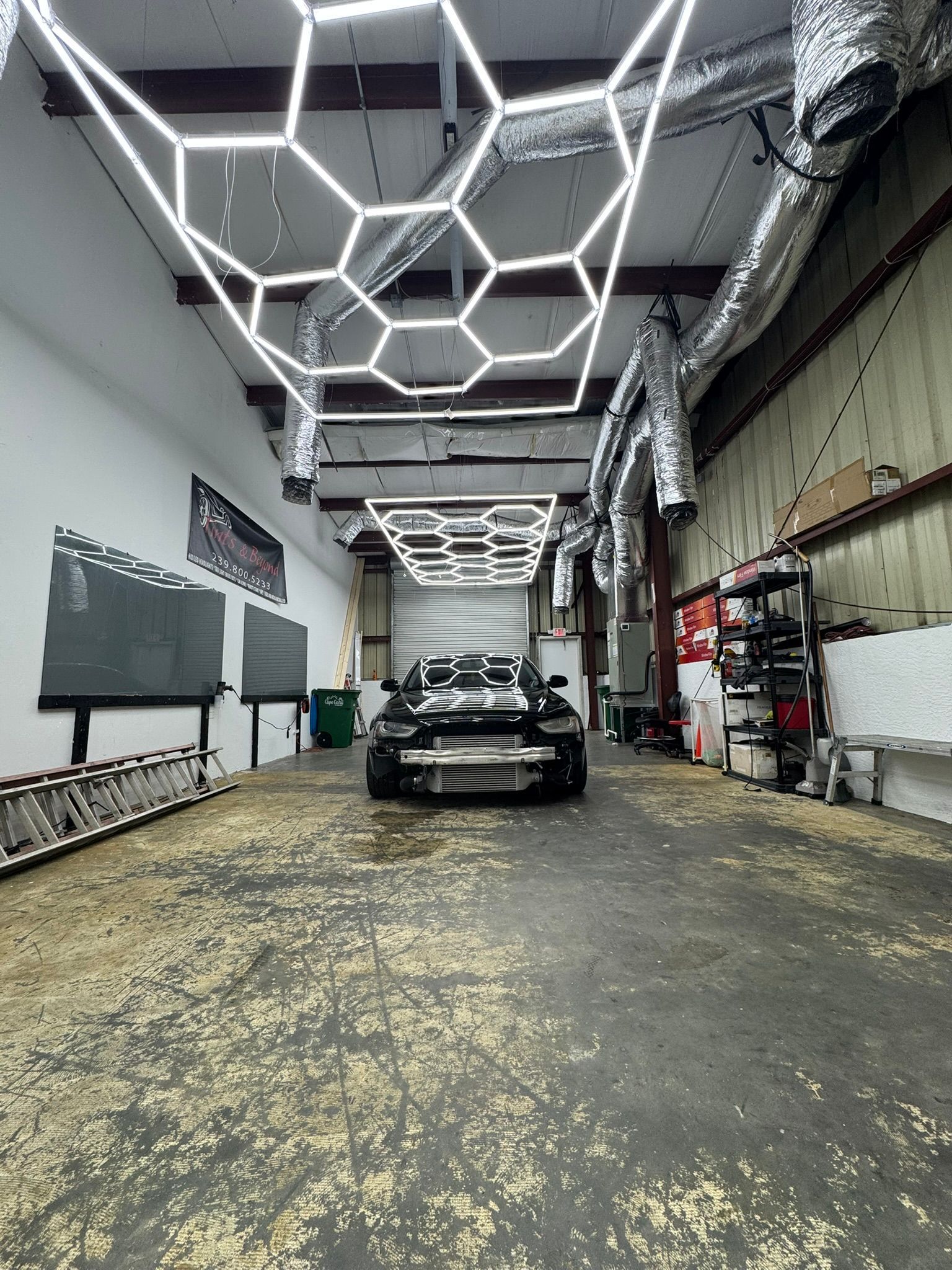 Black sports car in a garage with hexagon ceiling lights and industrial walls