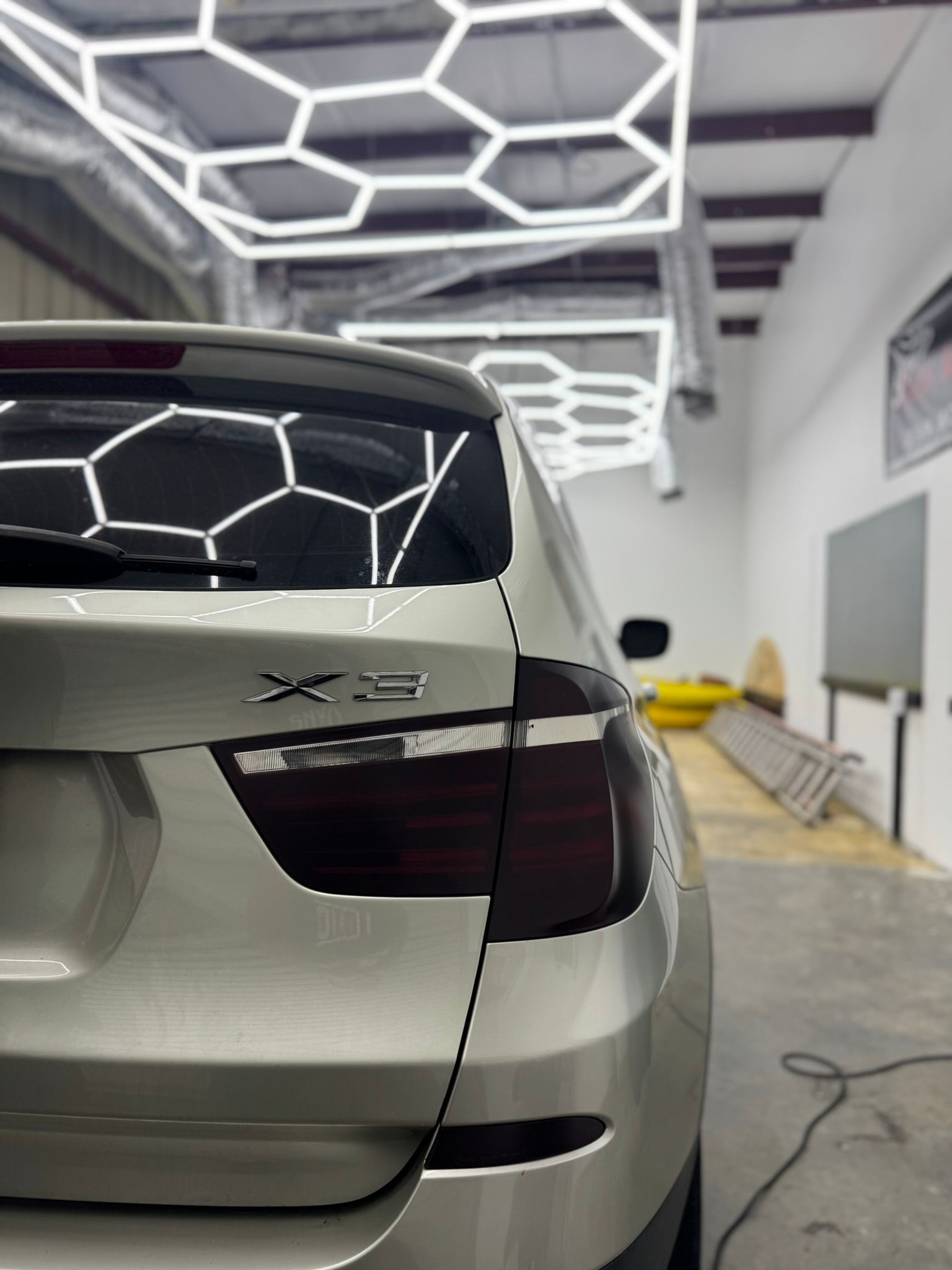 White SUV parked in a modern garage, rear view with geometric ceiling lights reflected on the back window.
