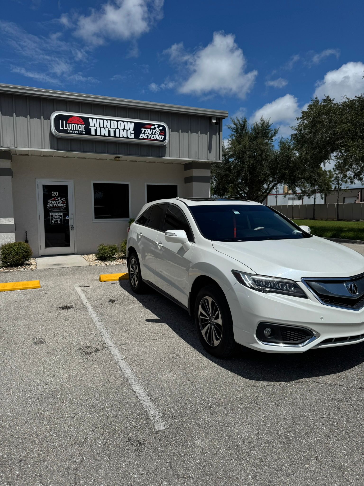 White SUV parked outside a small business under a blue sky.