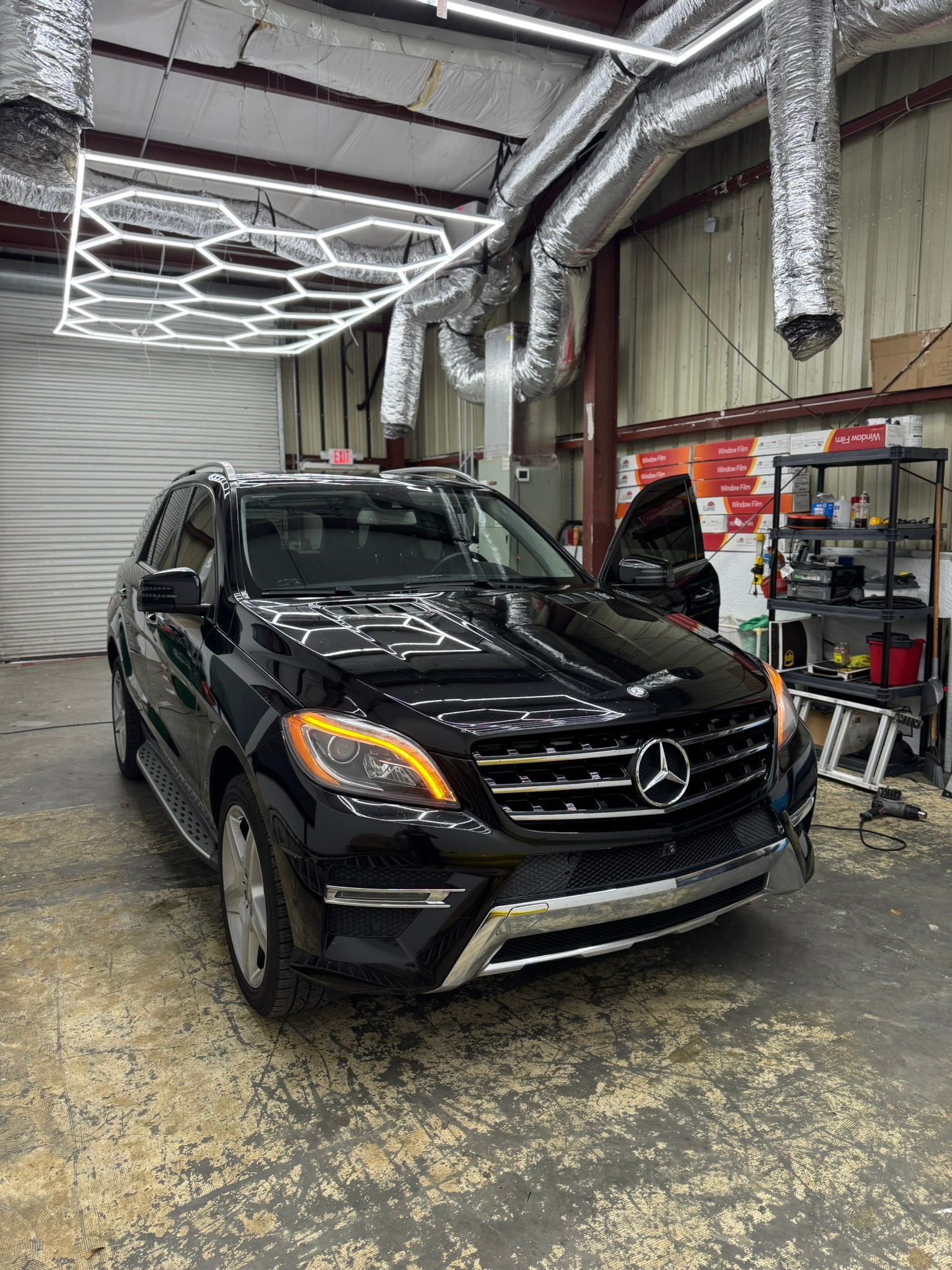 Black Mercedes SUV in an auto shop with a wet floor and overhead ventilation ducts.