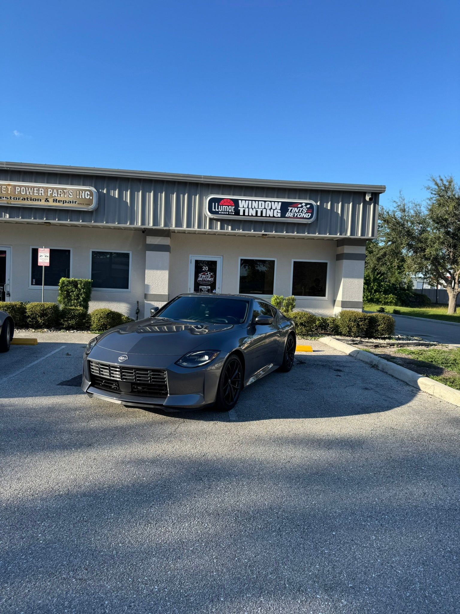 Black sports car parked in front of a small commercial building on a gravel lot
