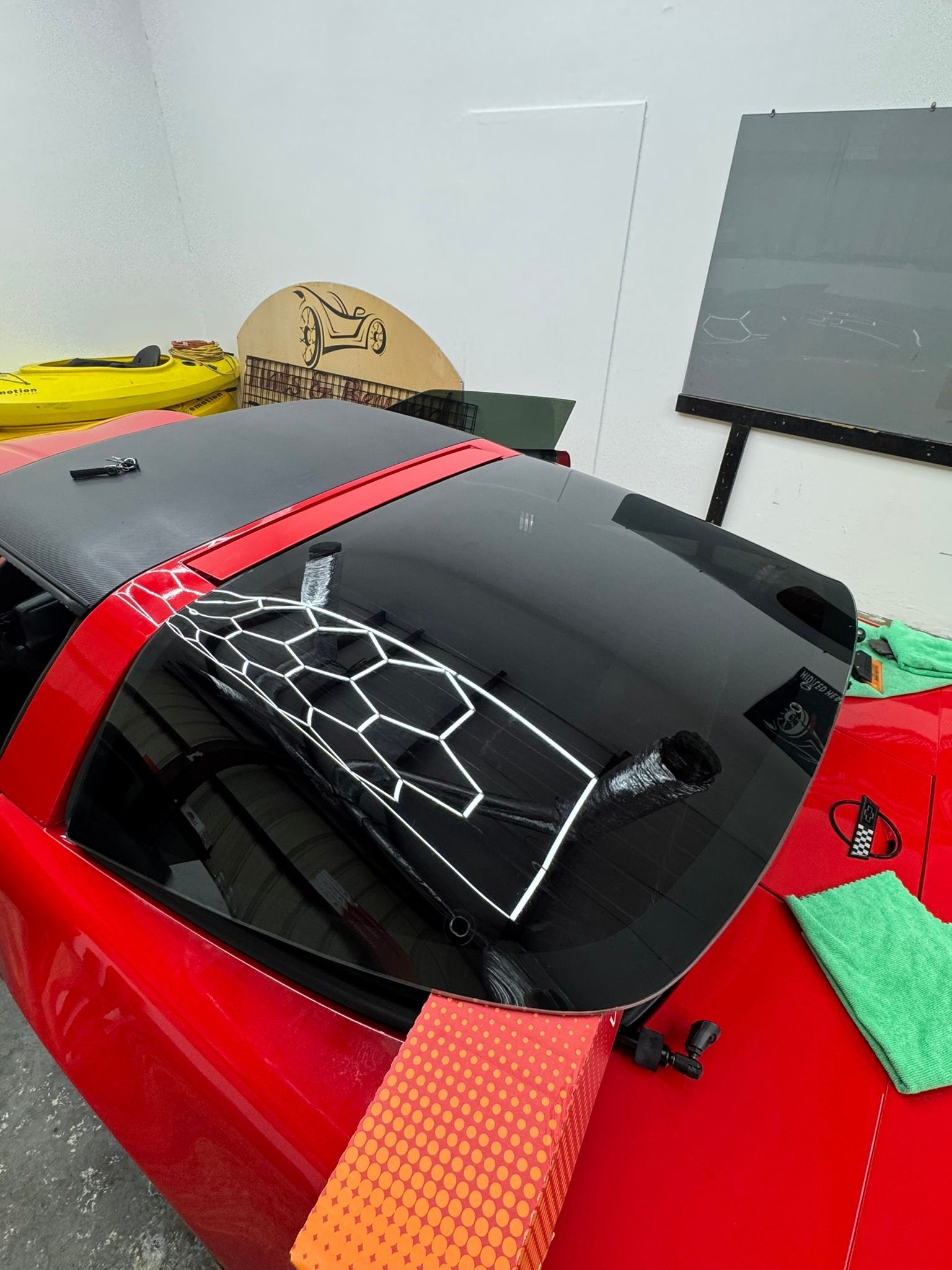 Red sports car in a garage with a red strap across the black roof and a cracked rear window area.