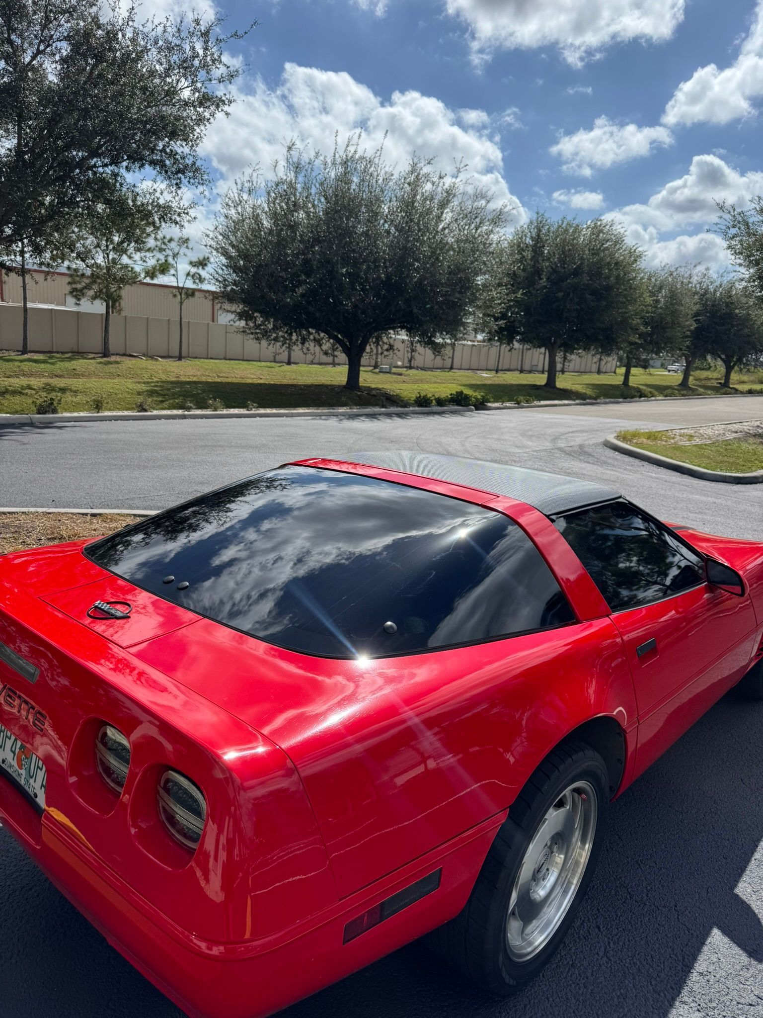 Red sports car parked on a street under a bright, partly cloudy sky.