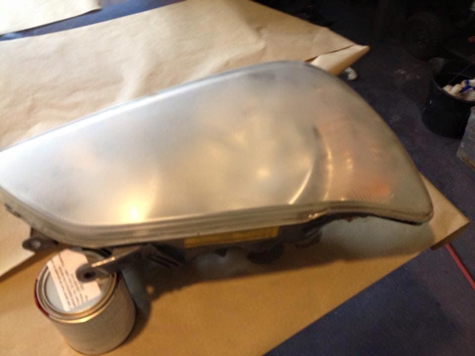 Silver motorcycle gas tank on cardboard, with a cap attached and a small container nearby.