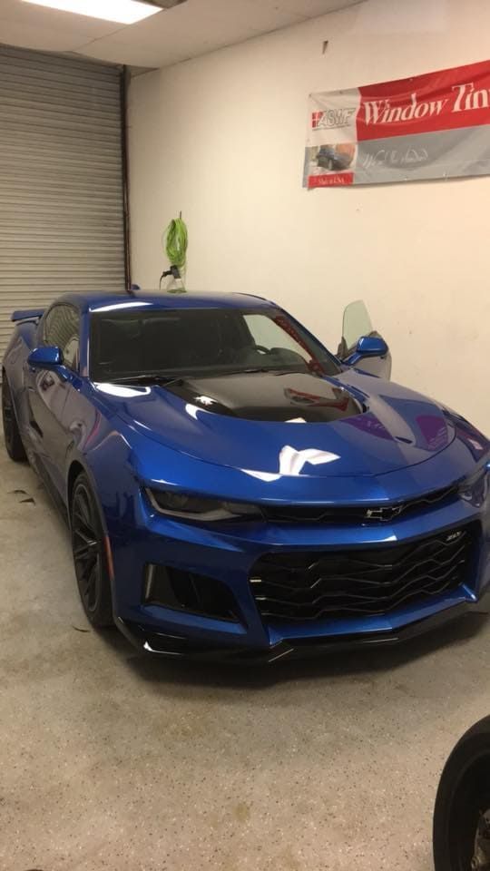 Blue sports car parked indoors under a “Welcome” banner.
