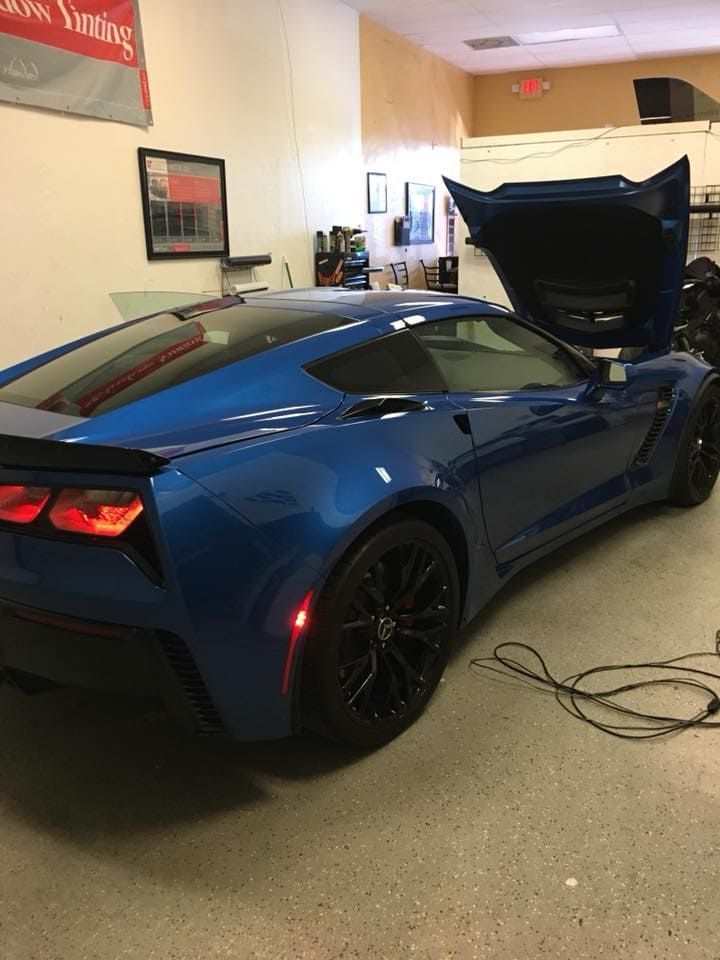 Blue sports car with its hood open in a garage or showroom, rear view with black rims and cables on the floor