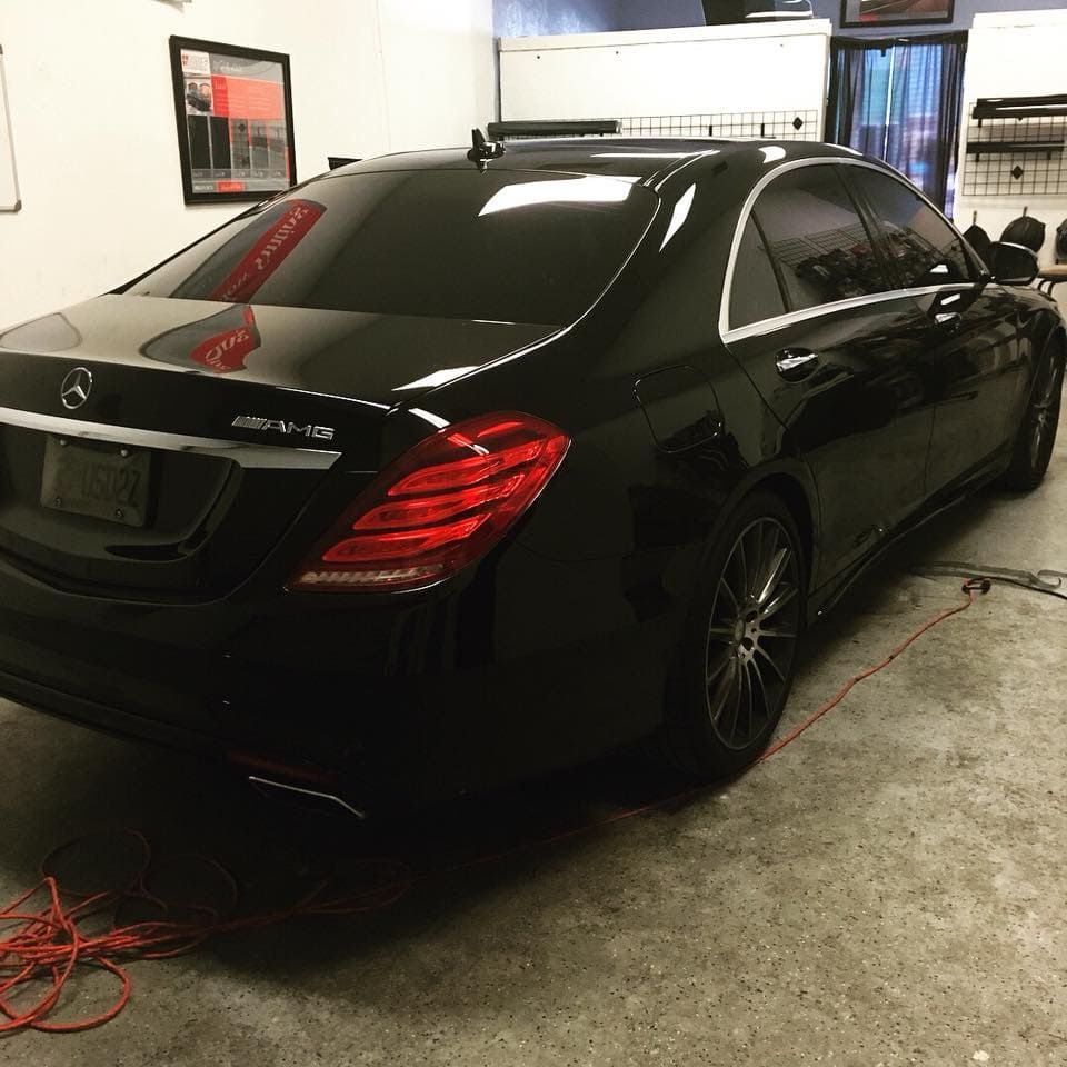 Black Mercedes sedan parked inside a garage, with a wall-mounted charger and red cables on the floor