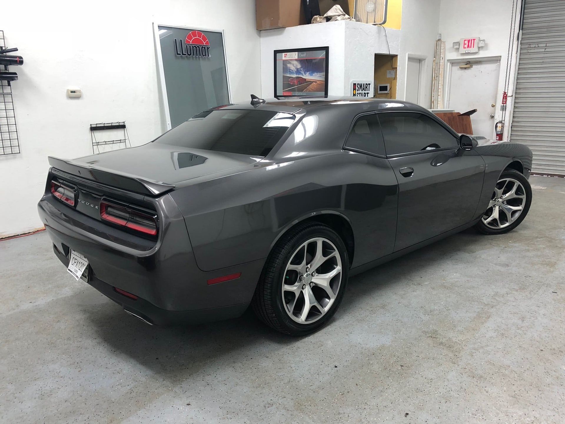Dark gray sports car parked in a garage, rear three-quarter view.