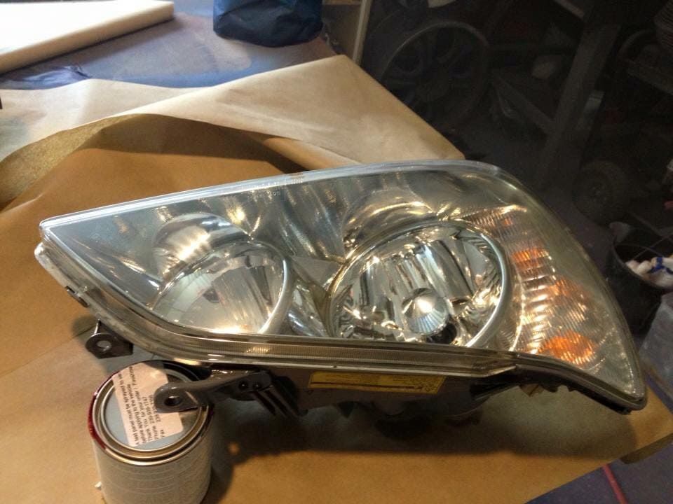 Car headlight assembly on a workbench with a roll of tape beneath it.