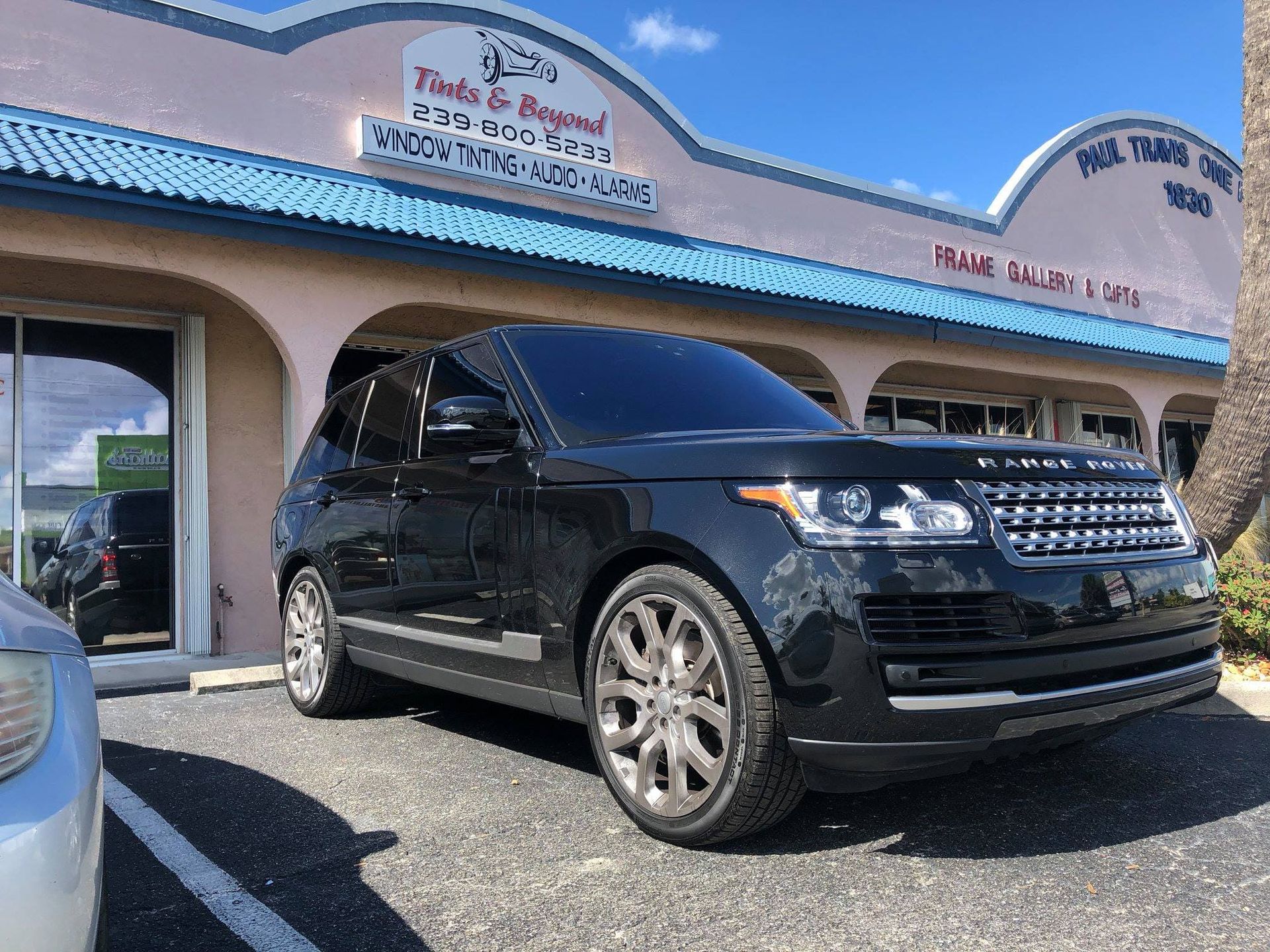Black SUV parked outside a storefront with a blue roof on a sunny day