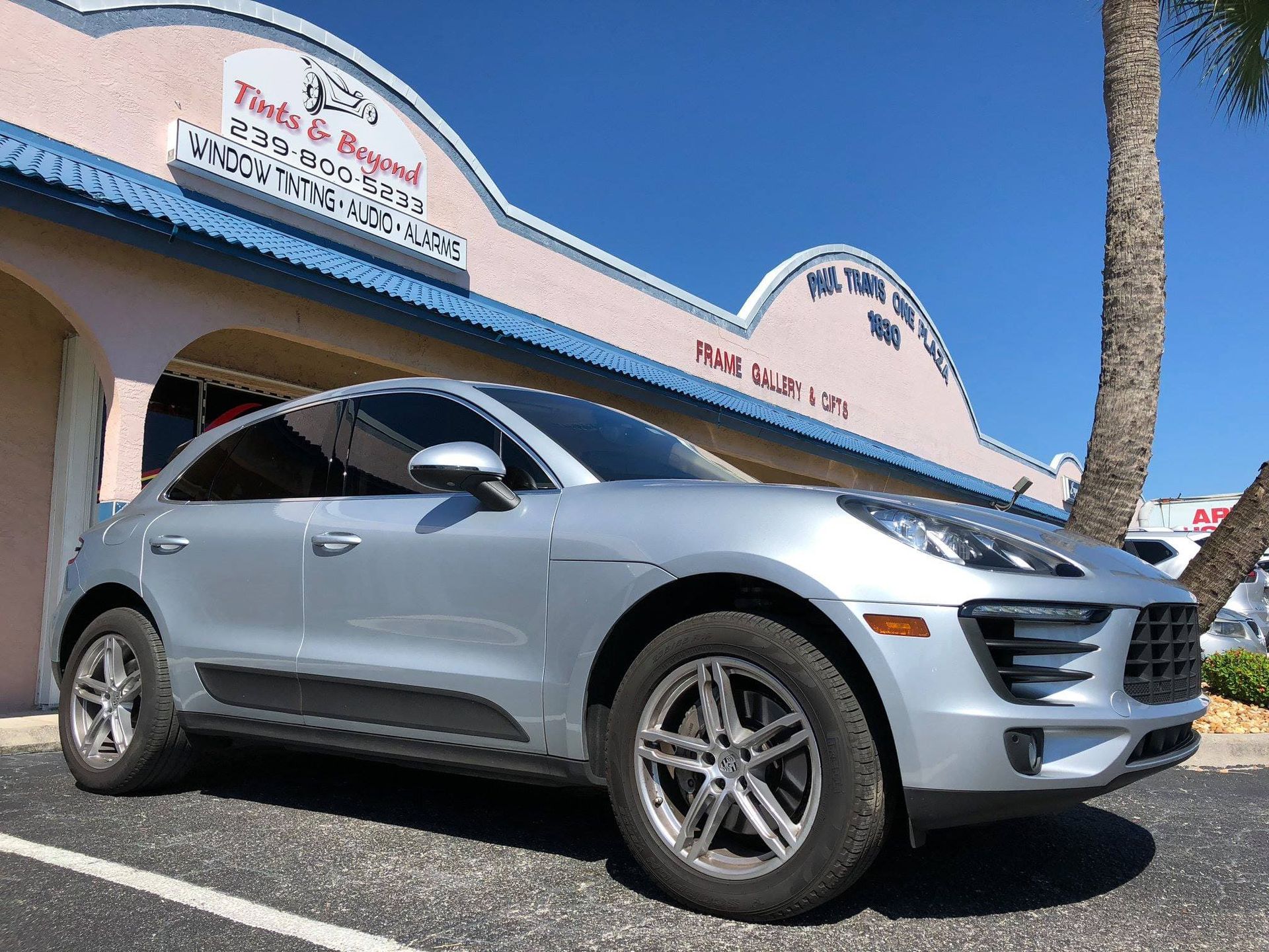 Silver SUV parked outside a business with a blue sky and palm tree.