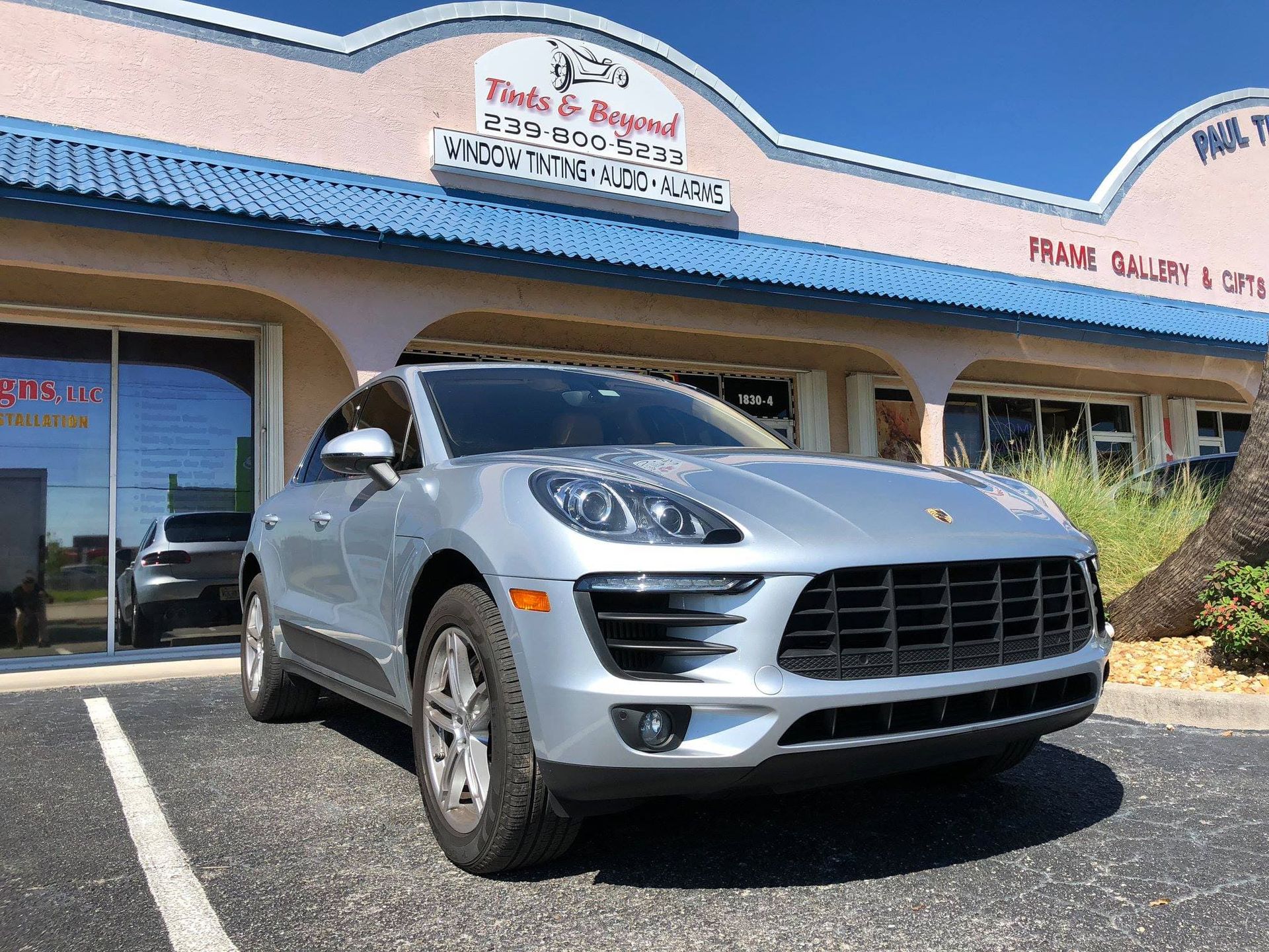 Silver Porsche SUV parked outside a storefront with blue awnings and a sign above the entrance