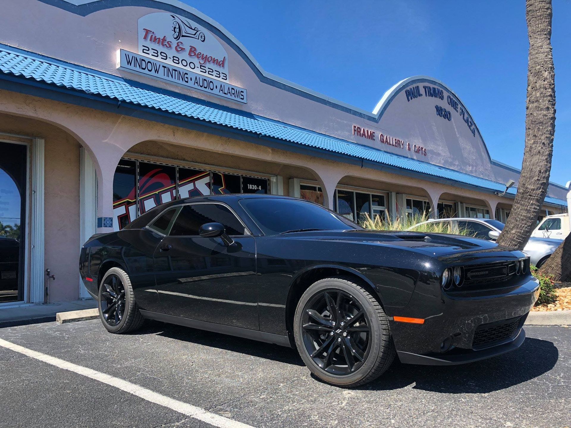 Black sports car parked outside a storefront with blue trim on a sunny day.