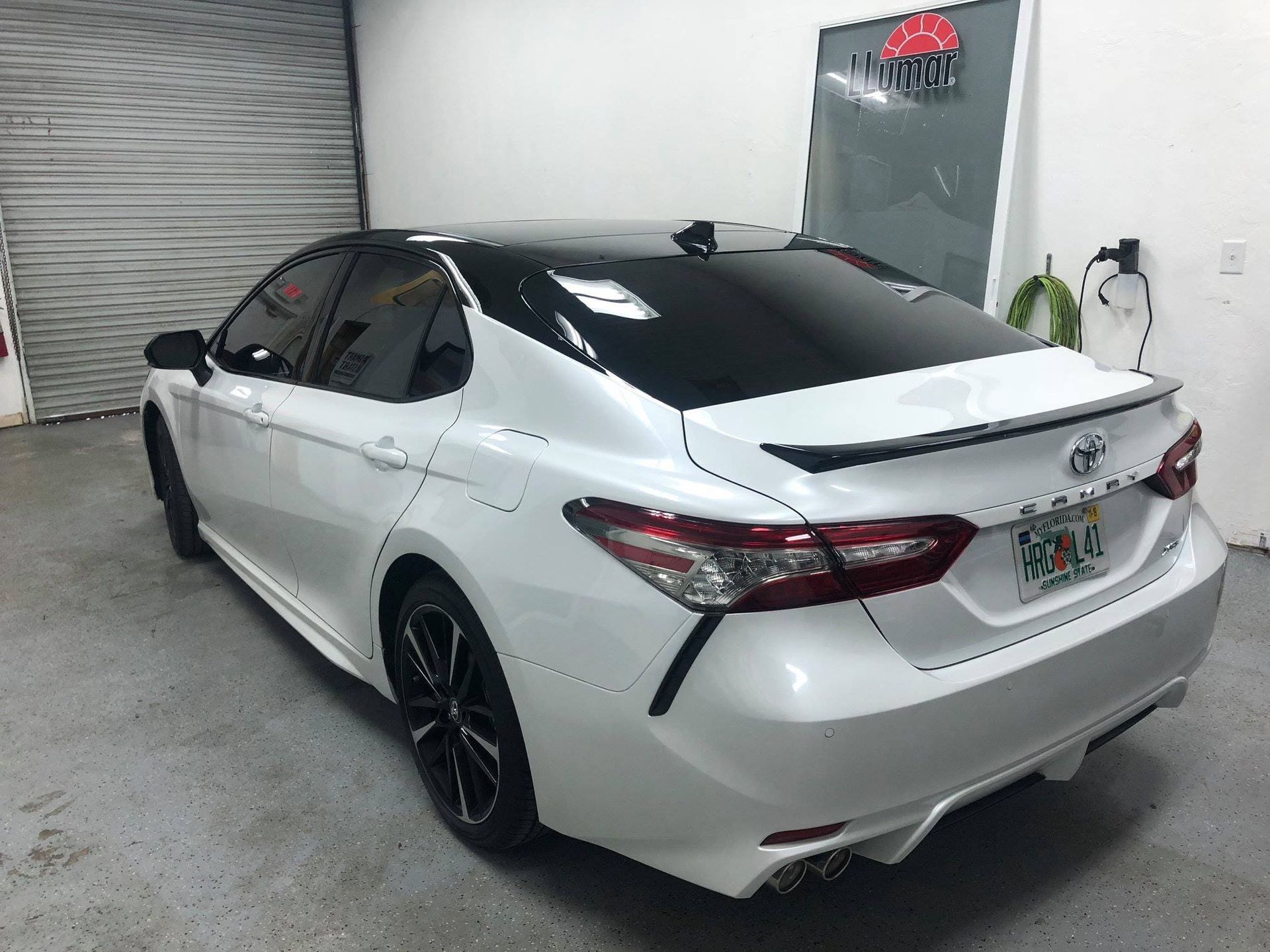 White Toyota sedan with black wheels parked in a garage, rear three-quarter view