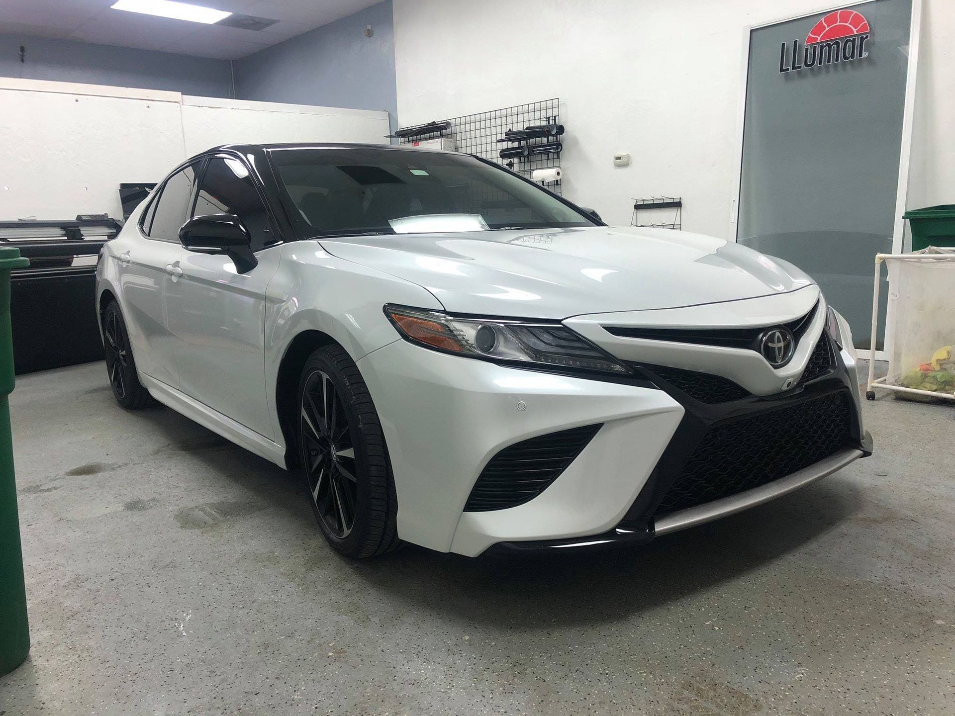 White sports sedan in an indoor garage, front three-quarter view on a speckled floor.