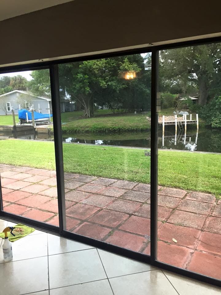Covered patio with red brick floor overlooking a green yard and pond through large sliding glass doors