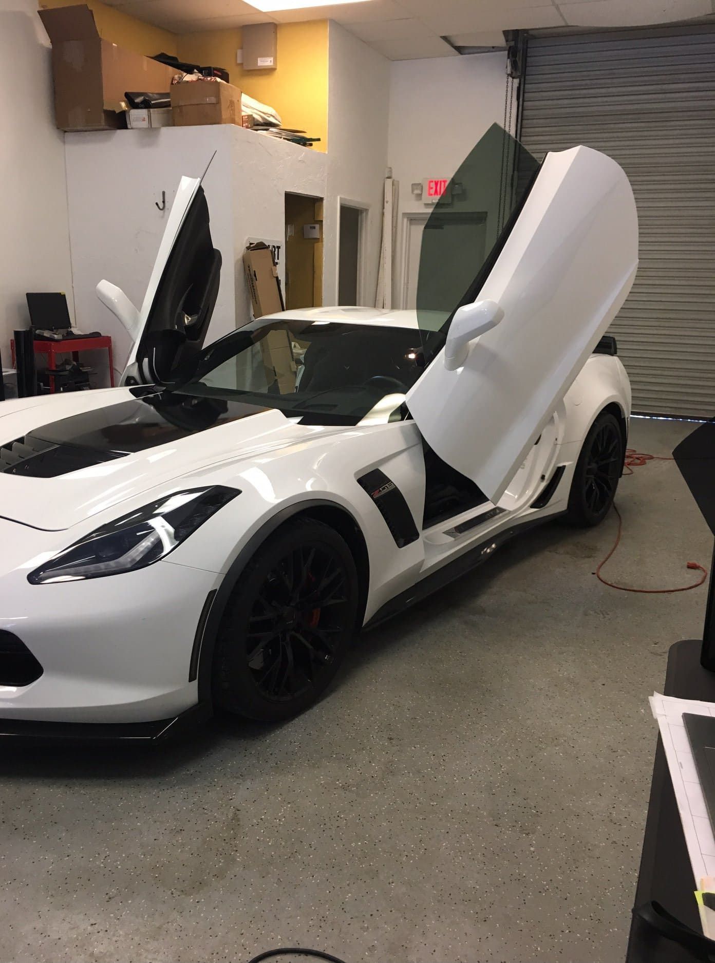 White sports car in a garage with both scissor doors open.