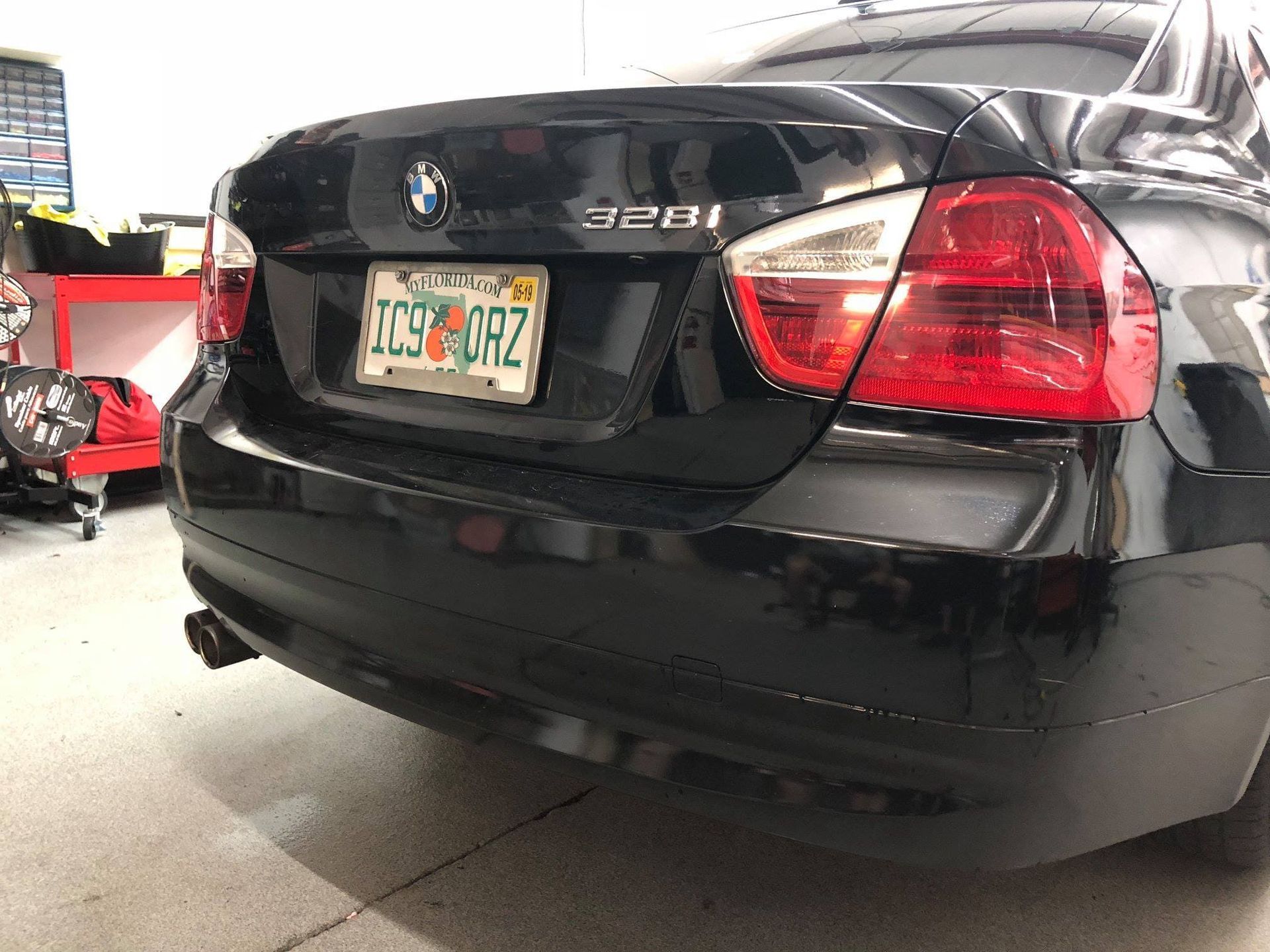 Rear view of a black BMW 328i parked in a garage, with a visible license plate and taillights.
