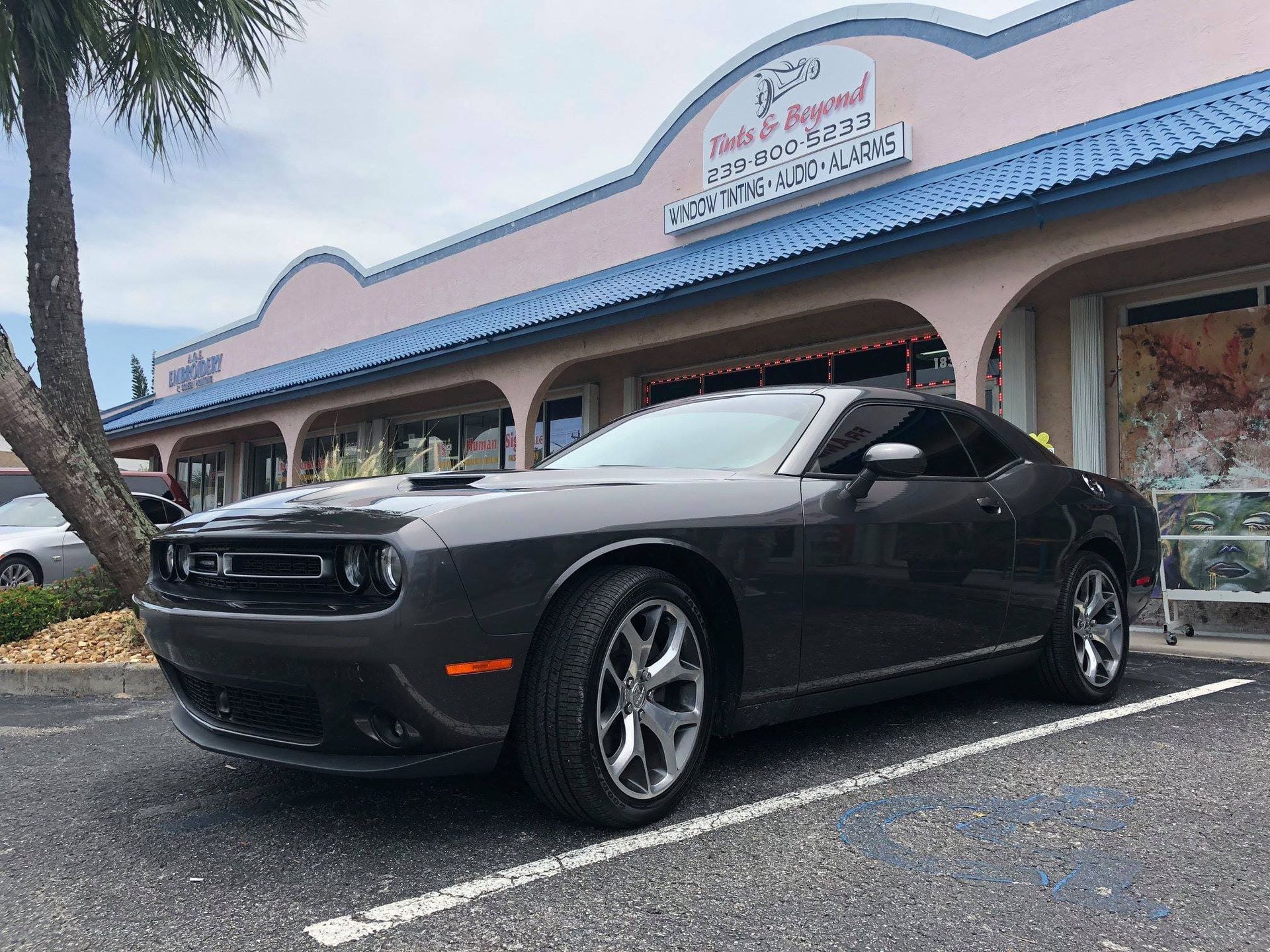Black Dodge Challenger parked outside a storefront with blue awning and mural wall