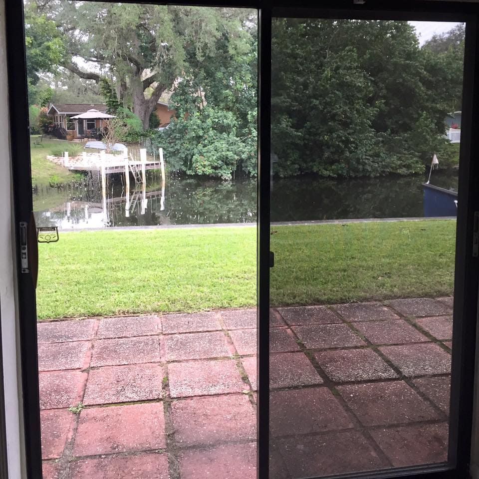 Sliding glass door opens to a backyard with patio tiles, green lawn, and a pond with a small dock.