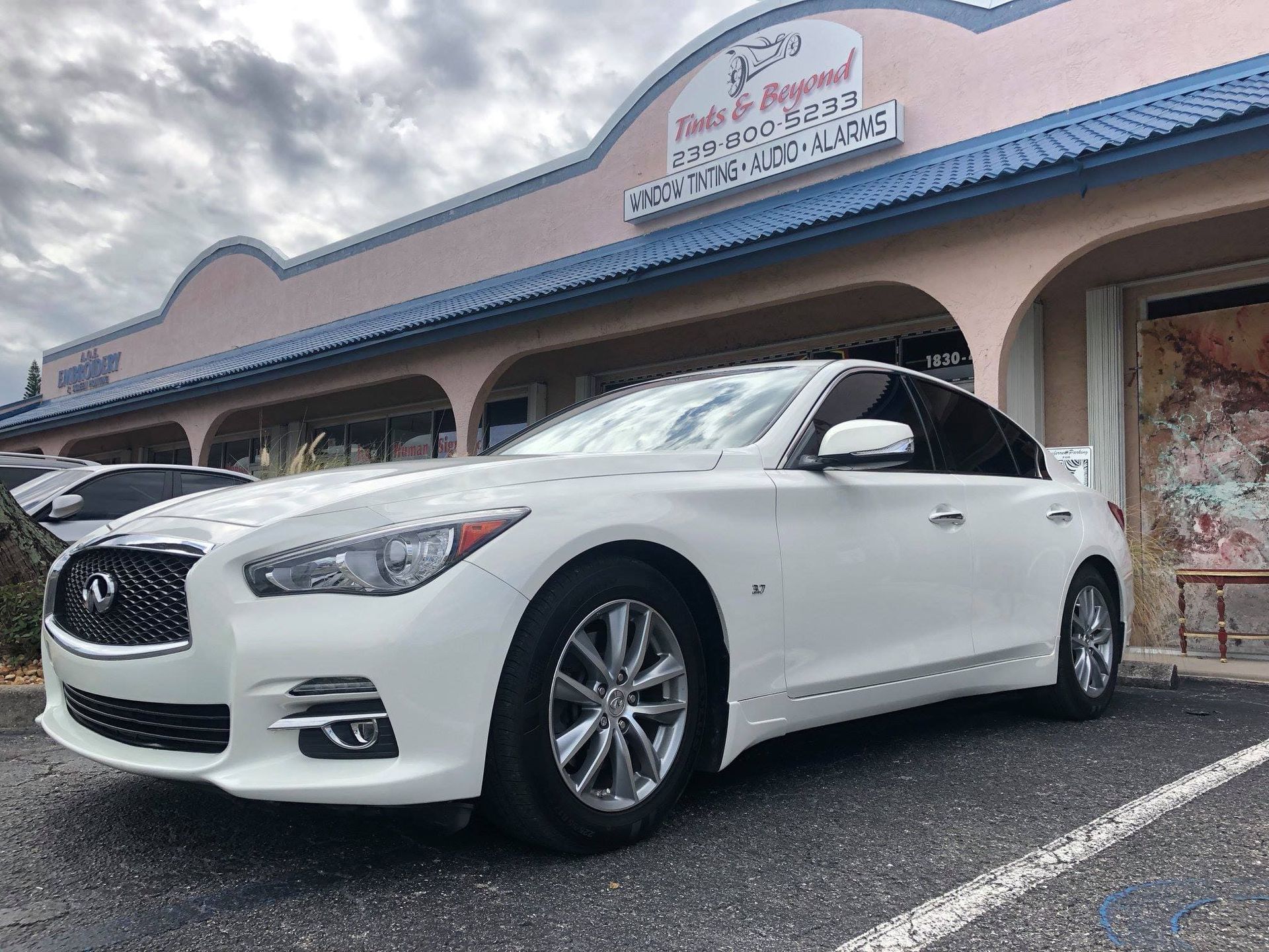 White sedan parked outside a strip mall storefront under a cloudy sky
