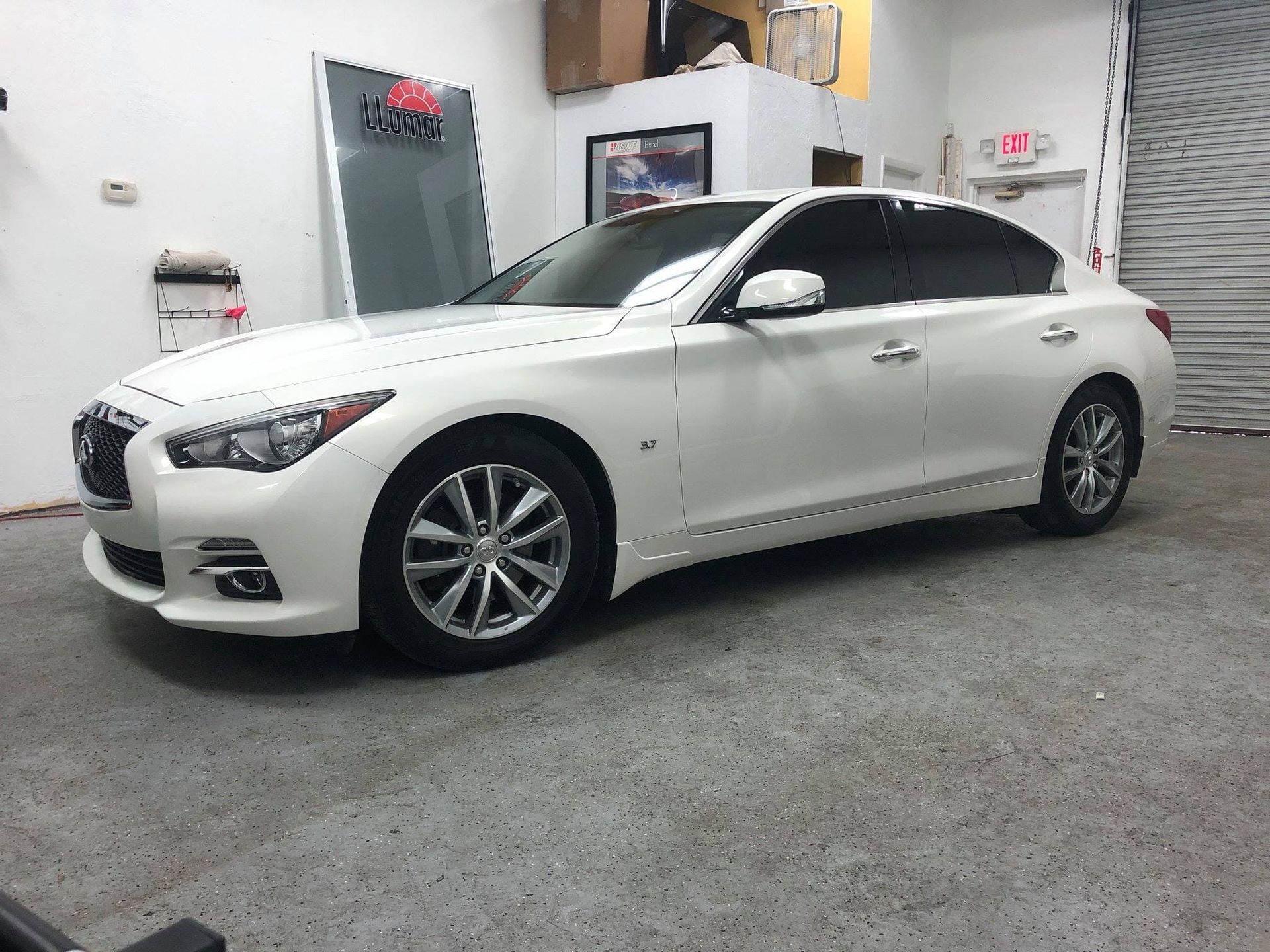 White sedan parked inside a garage with a concrete floor and workshop walls