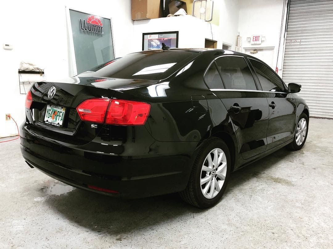 Black sedan parked in a garage, viewed from the rear-left side