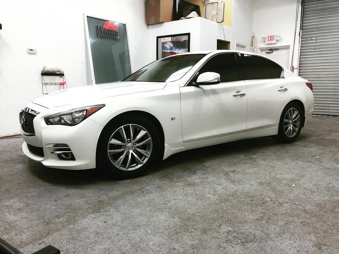 White sedan in a garage or showroom, viewed from the side with the roof open.