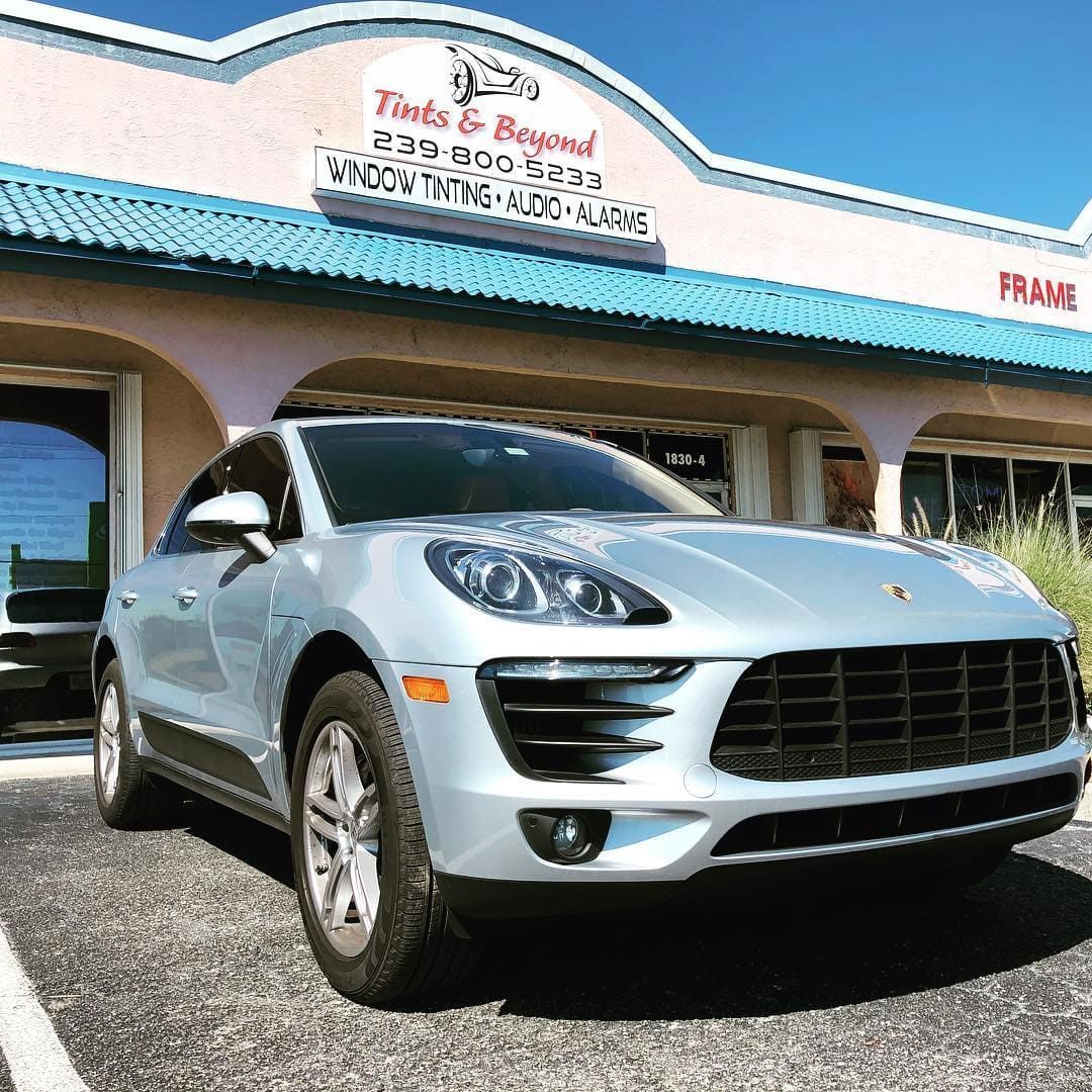 Silver Porsche SUV parked outside a business with a blue roof under a clear sky