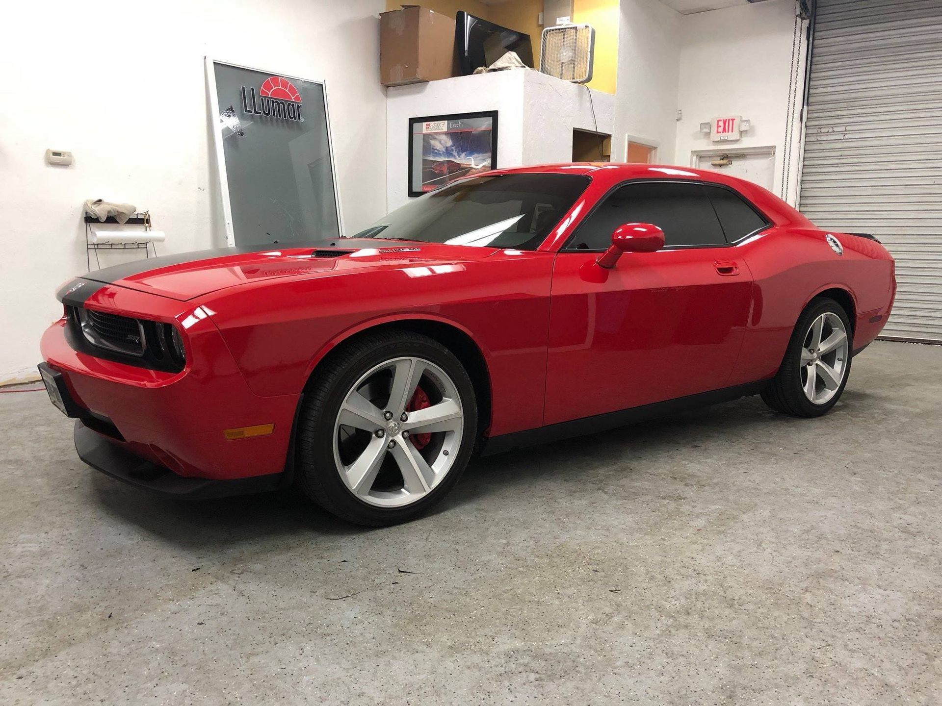 Red Dodge Challenger in a garage, viewed from the side, with shiny red paint and silver rims