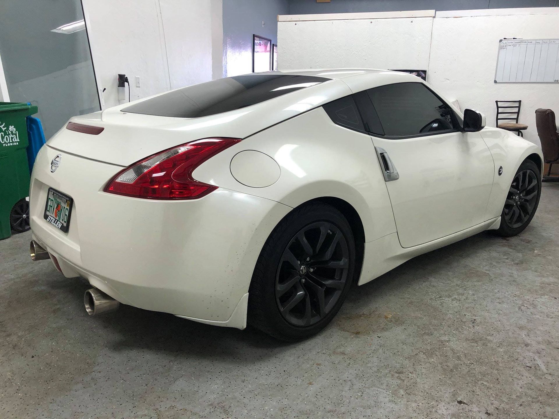 White sports coupe with black wheels parked in a garage, rear three-quarter view
