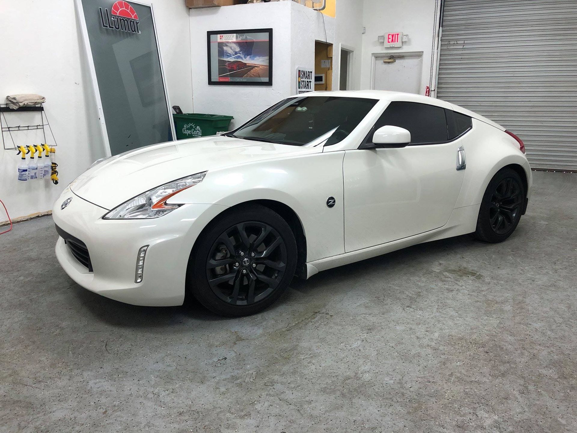 White sports coupe with black wheels parked inside an auto shop garage.