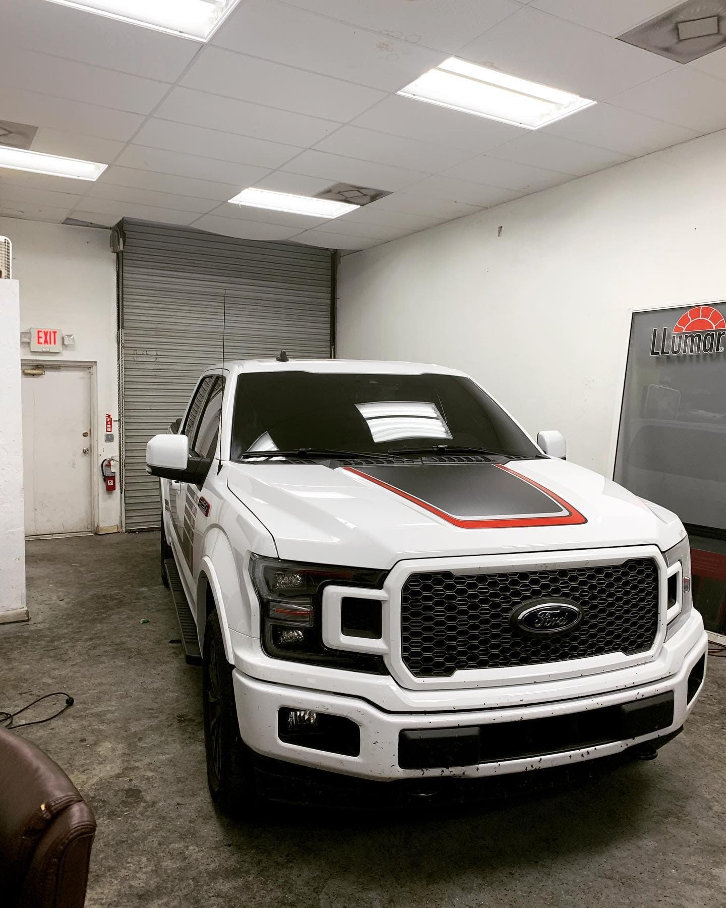 White Ford pickup truck in a garage, with black hood and red trim accents.