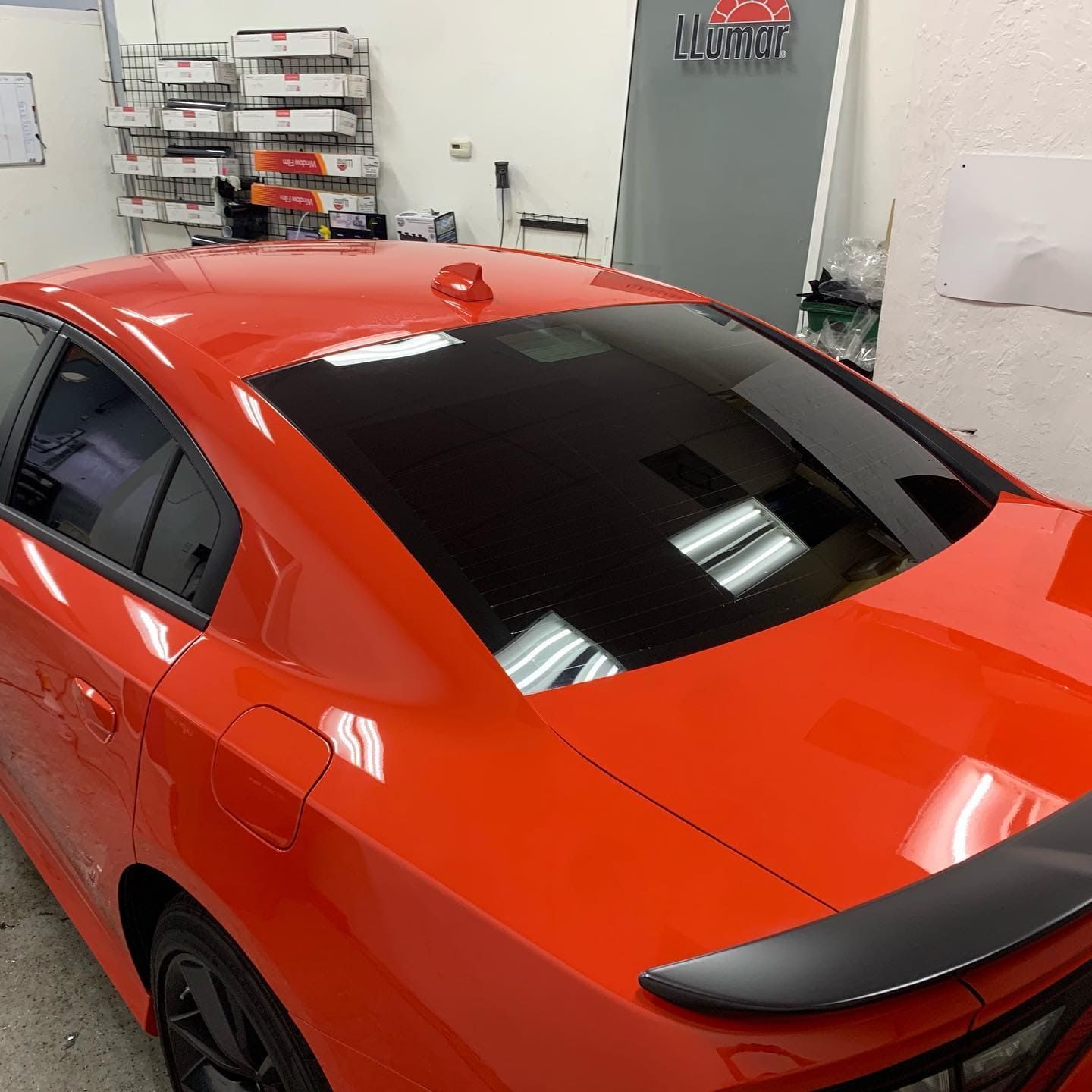 Orange sports car in a garage, viewed from the rear side with tinted windows and a black spoiler.