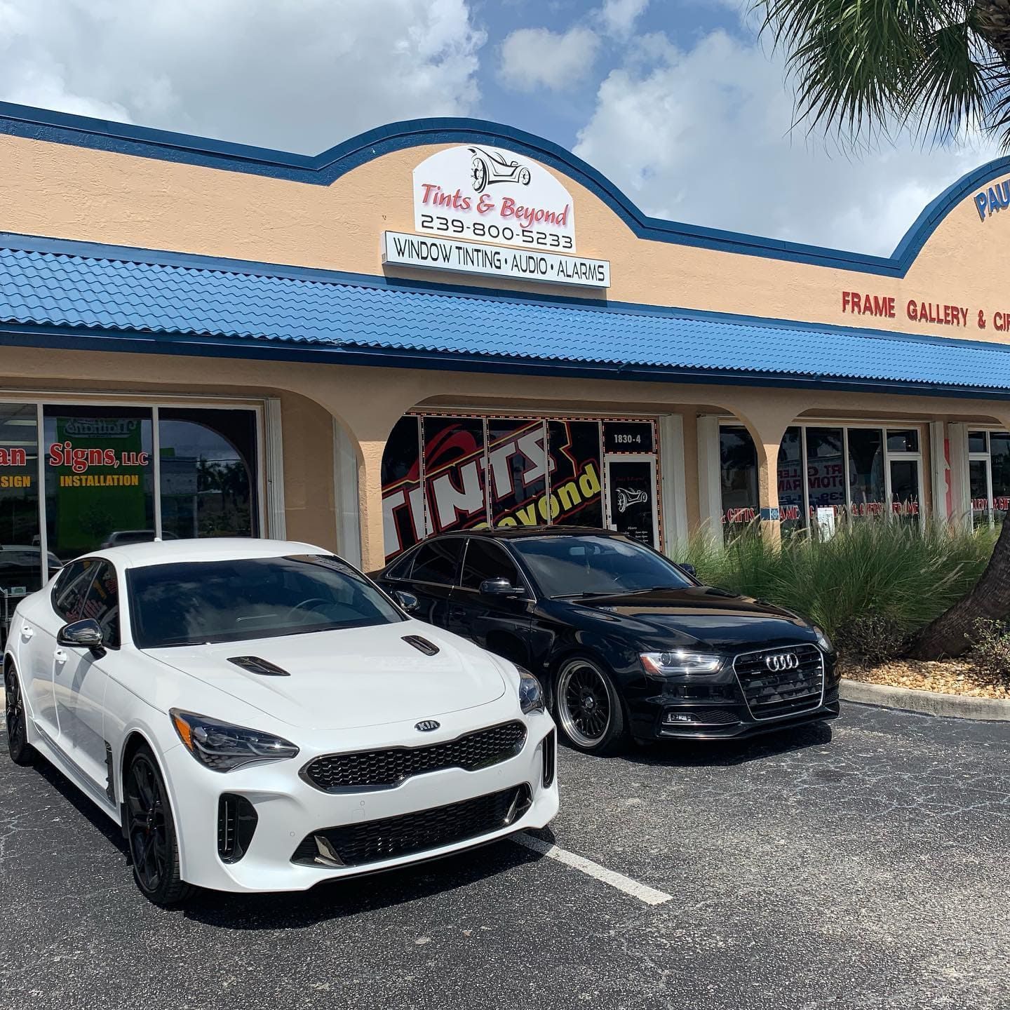 White and black sports cars parked outside a blue-roofed shop with “Tires & Rims” sign