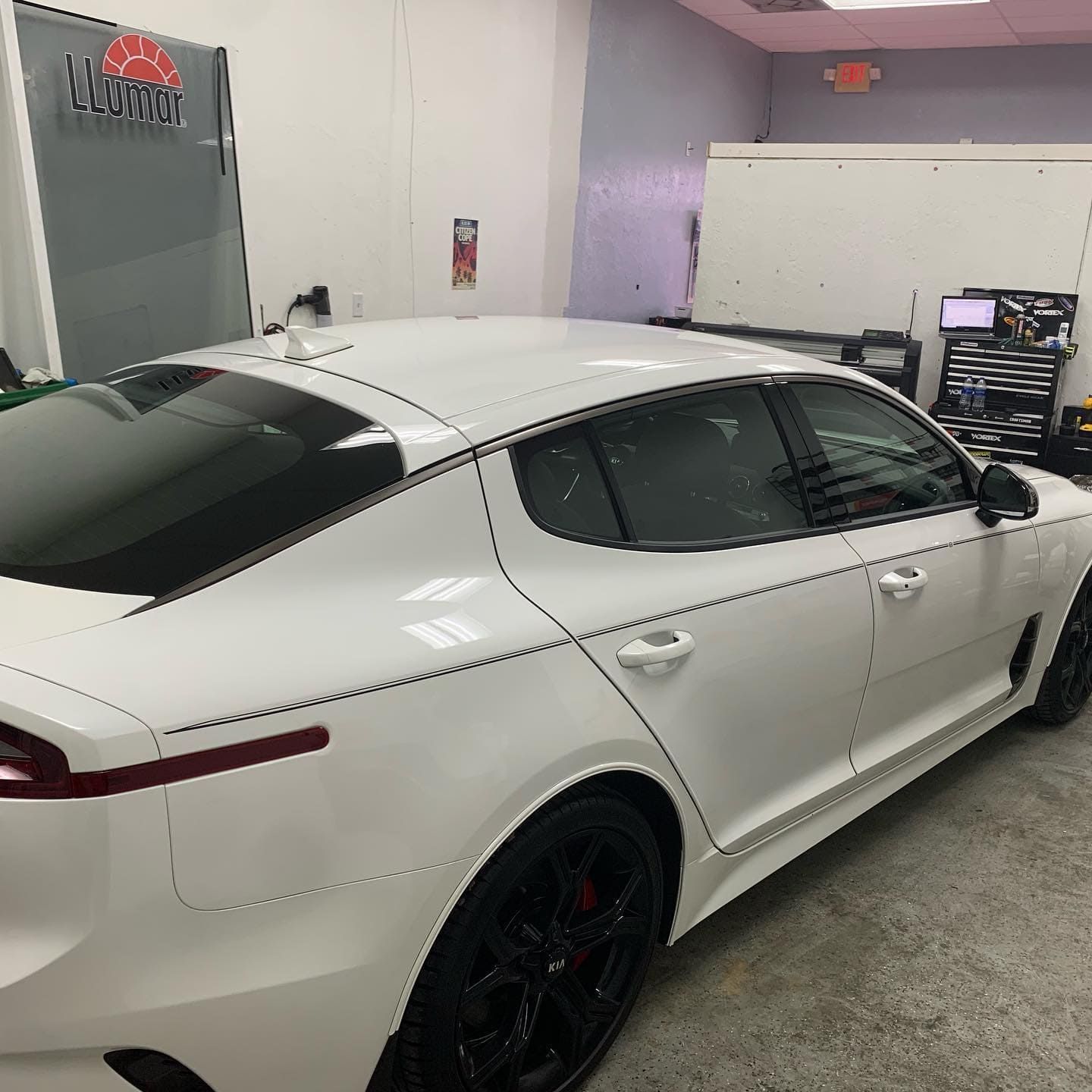 White sedan with tinted windows and black rims parked indoors in a garage or detailing shop.