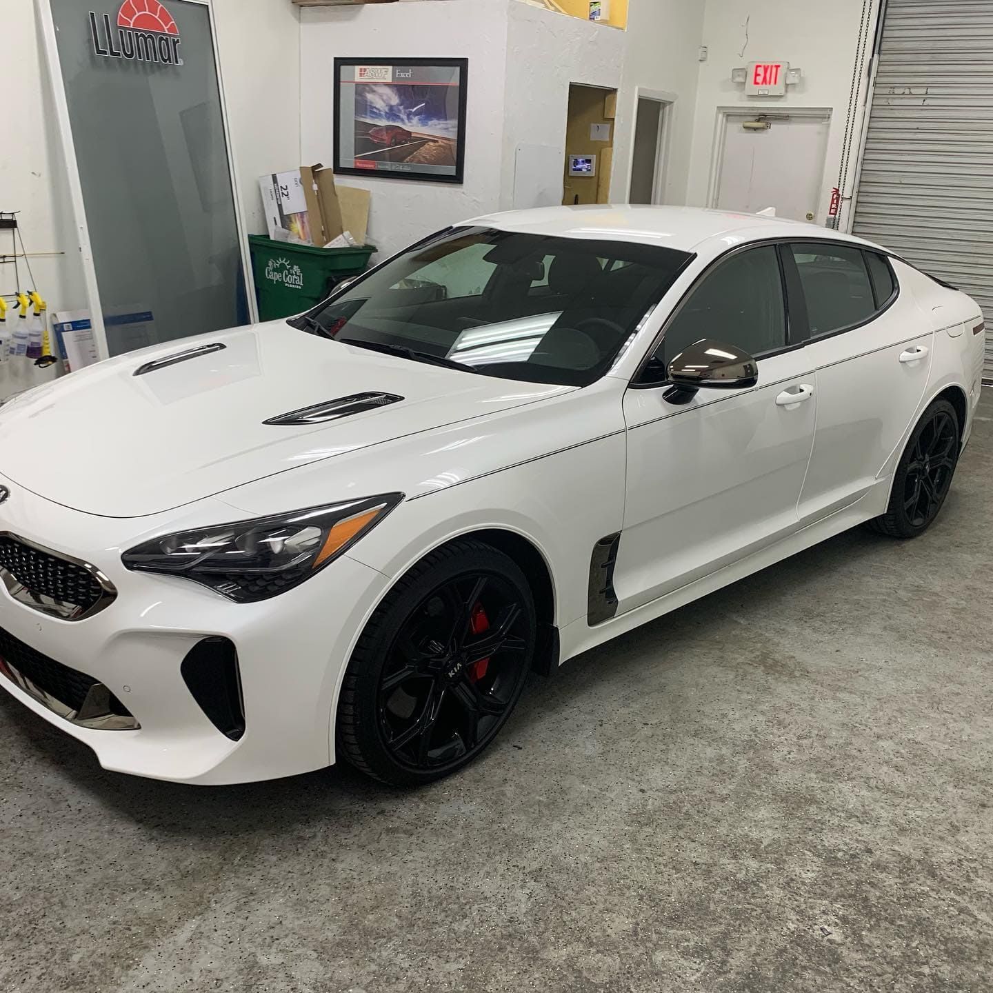 White sports sedan in a garage, angled front view with black wheels and red brake calipers.