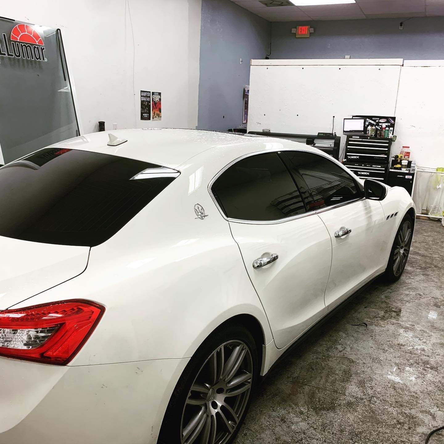 White sedan parked inside a garage with wet concrete floor and white walls